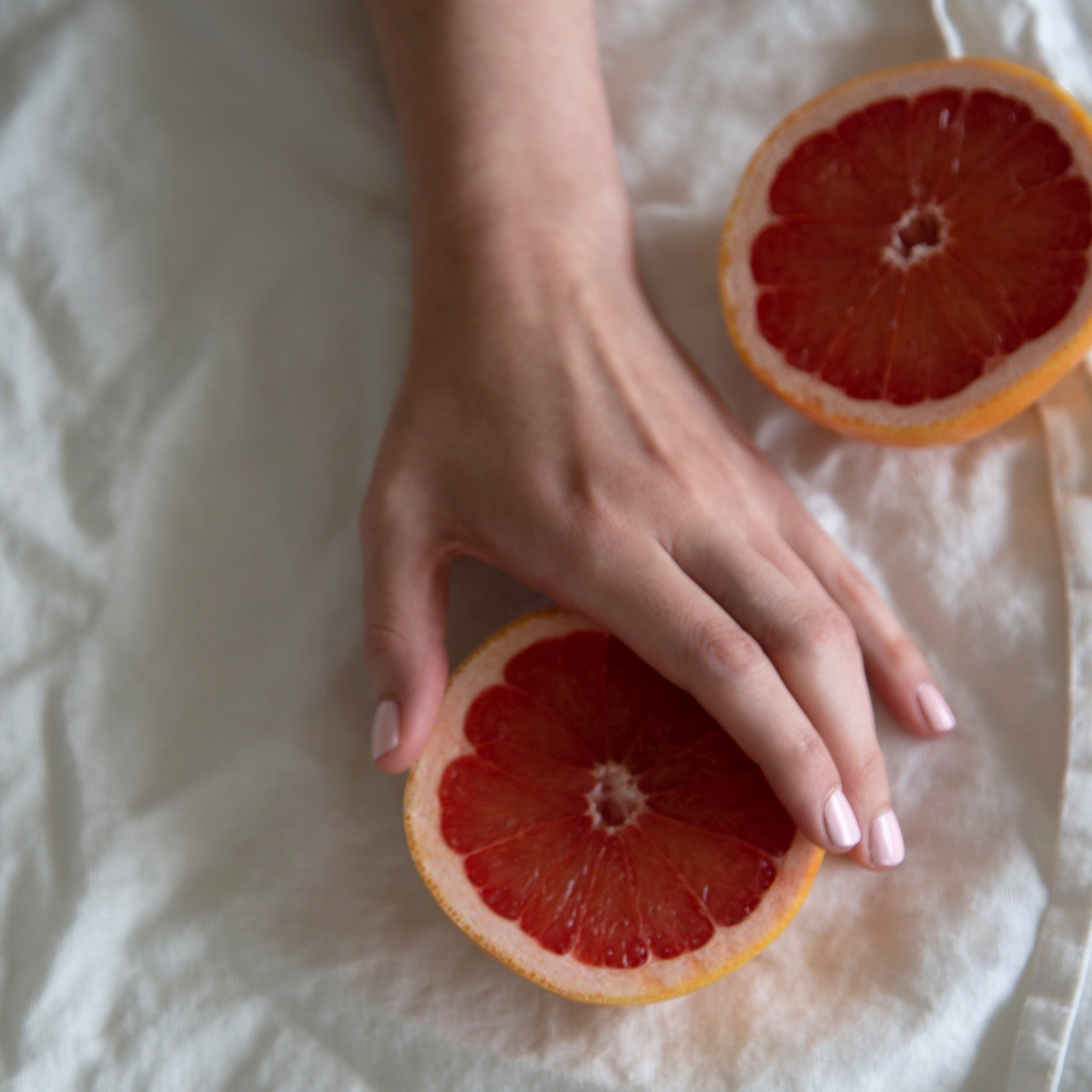 A female hand clutching a sliced grapefruit, wearing Powder Pink a light baby pink shade of nail polish 
