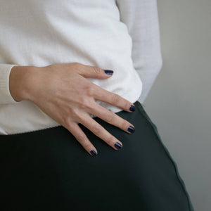 A female stretching out her hand, wearing Midnight Sky nail polish, a dark blue shade.