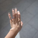 A caucasian female hand in the sunlight wearing Cloud Mist, a medium to light grey silvery nail polish