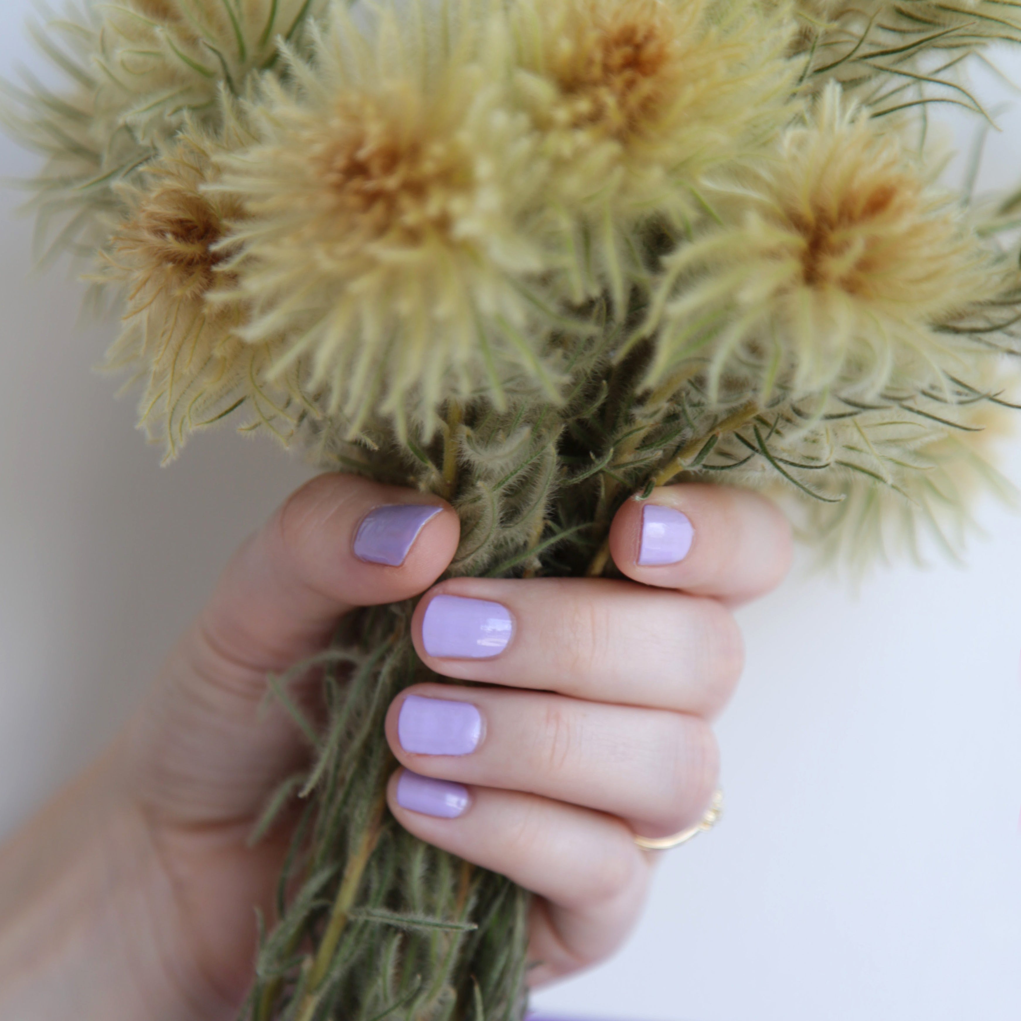 A female holding a bunch of flowers, wearing Lilac Fizz a purple shade of nail polish