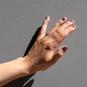 A female hand against a dark backdrop, wearing Sangria, a medium to dark pink nail polish