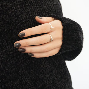 A female hand resting on her dark sweater, wearing Volcanic Ash a dark grey nail polish by Paint nail Lacquer