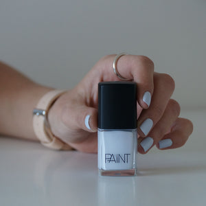 A female holding a bottle of Pale Glacier nail polish, wearing the same colour on her nails, the colour is light blue