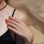 A female laying on the beach with a sandy hand, wearing Coral Sunset nail polish a bright warm orange shade