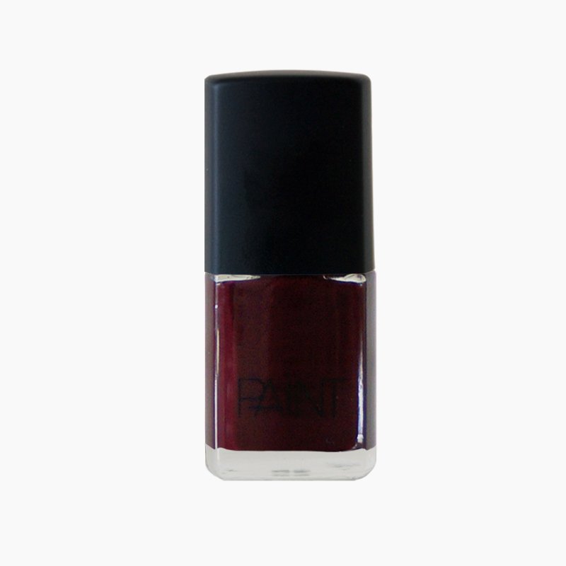 A bottle of lady voodoo nail polish by Paint Nail Lacquer against a white backdrop, this shade is a dark red with black and gold undertones 