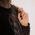 A female holding her gold necklace whilst wearing Midnight Sky a dark blue nail polish