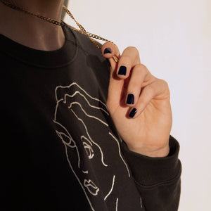 A female holding her gold necklace whilst wearing Midnight Sky a dark blue nail polish