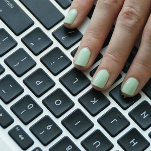 A caucasian female's hand wearing Mint Sorbet Nail Polish by Paint Nail Lacquer resting on a black computer key board.