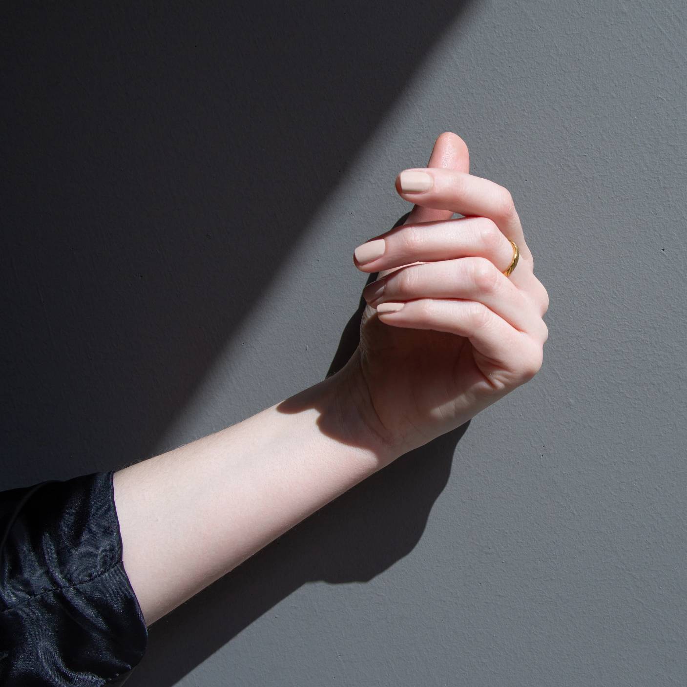 A female with her hand against a dark backdrop but in the sunlight, wearing Paint Naked nail polish a light nude shade of brown