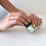 A caucasian female's hands wearing mint sorbet Nail Polish by Paint Nail Lacquer holding a bottle of the same nail polish.