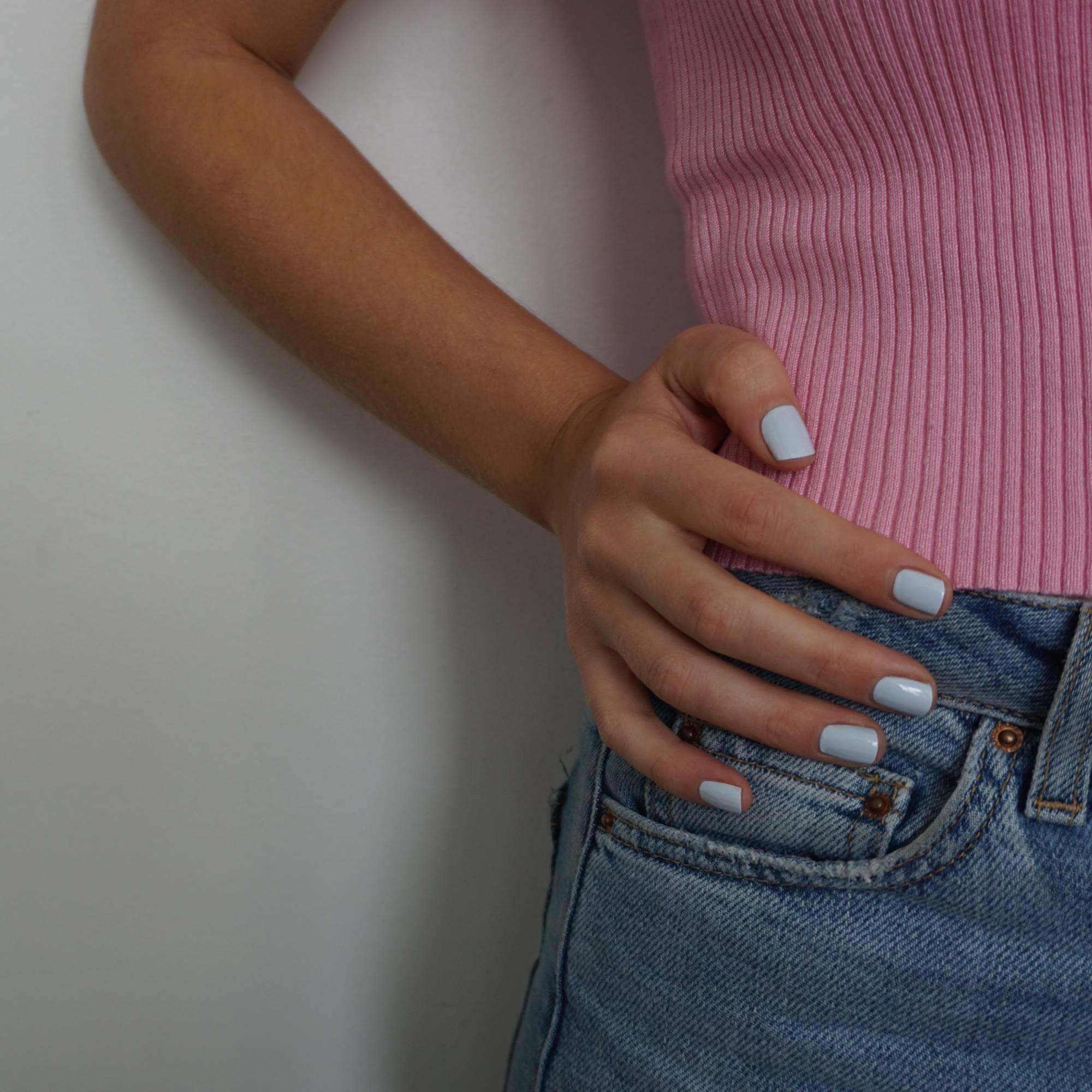 A female hand on hip, wearing Pale Glacier a baby blue nail polish, contrasting against her pink top and denim skirt.
