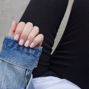 A female hand with fingers curled over denim jacket sleeve, wearing Powder Pink a light baby pink nail polish colour
