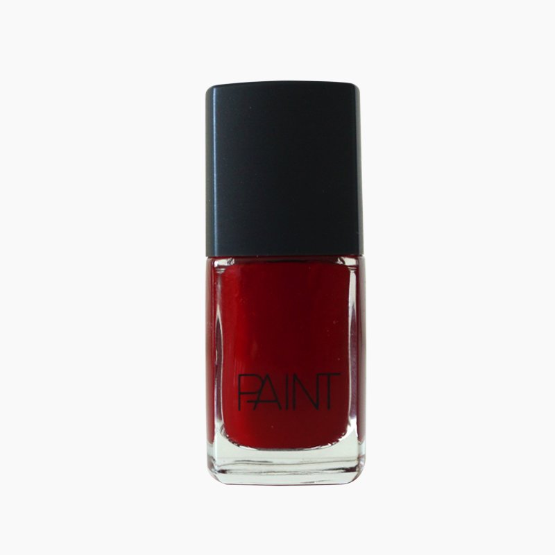 A bottle of Scarlet venom nail polish by Paint Nail Lacquer against a white backdrop, this shade is a dark red in colour