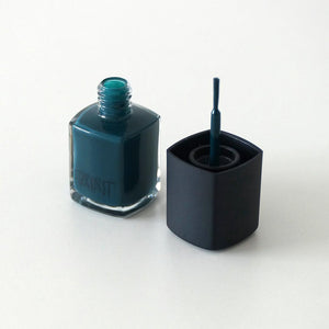 An open bottle of Sea queen nail polish by Paint Nail Lacquer showing the brush against a white backdrop, this shade is a dark teal green.