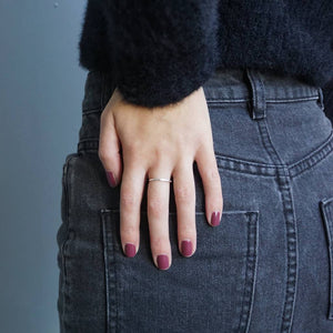 A female's hand resting on her backside wearing Velvet Berry nail polish, a dark pink shade. Contrasting against her faded black denim jeans.