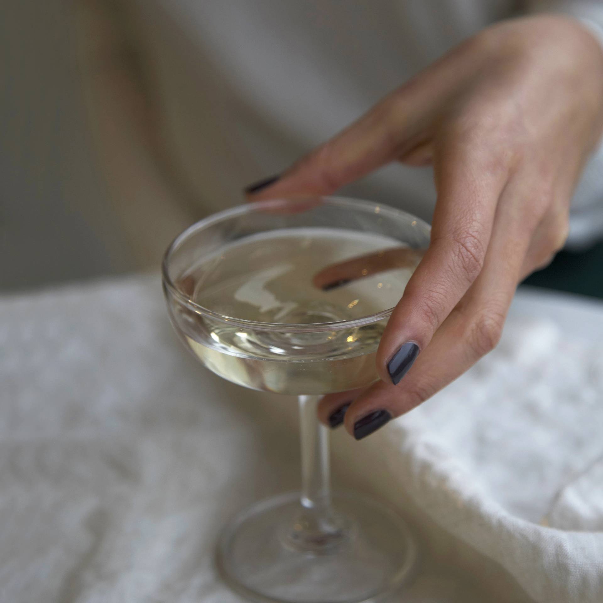 A female holding a glass of champagne, wearing Volcanic Ash a dark ash grey nail polish 